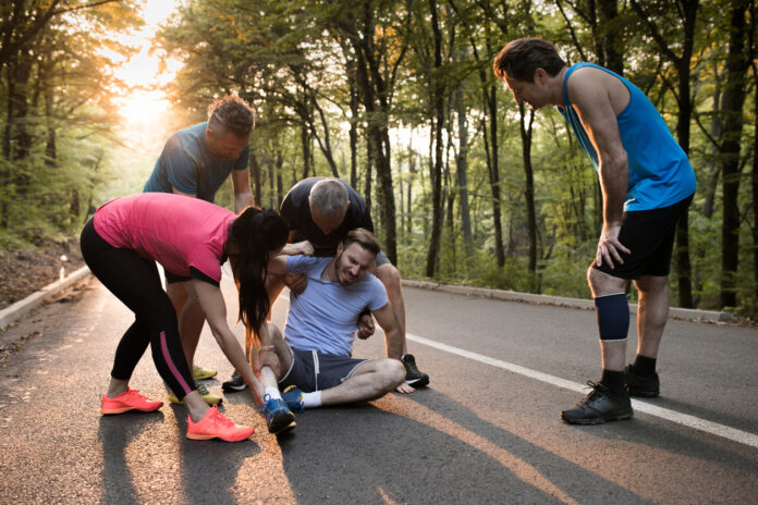 Group of athletes helping injured man during marathon race.
